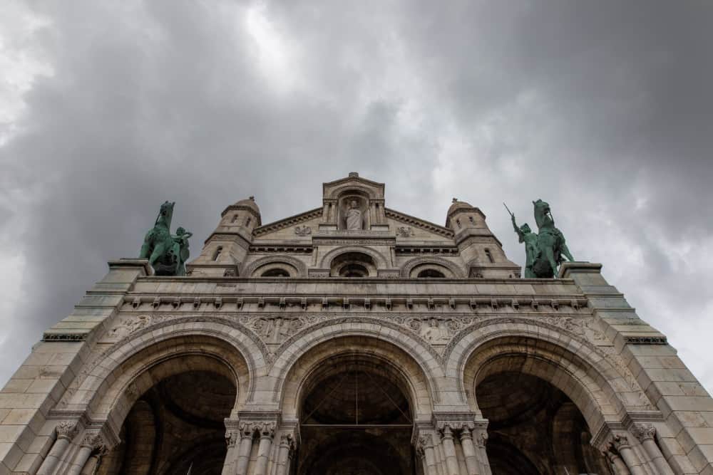 Die Basilika Sacré-Coeur, ein kunstvolles Gebäude in Montmartre, erhebt sich hoch unter einem bewölkten Himmel.