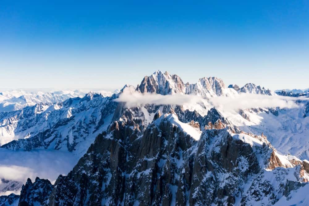 Ein atemberaubender Blick auf den schneebedeckten Mont Blanc, der über einer majestätischen Bergkette thront, während flauschige Wolken den Himmel bemalen.